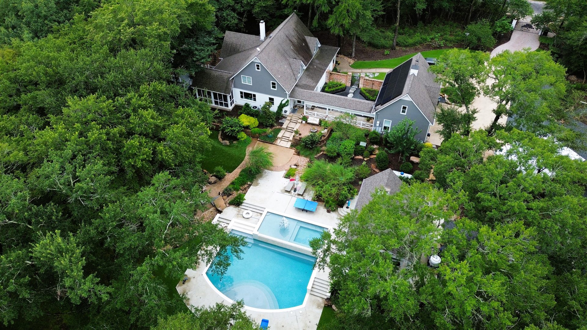 Aerial view of a wooded estate with pool and landscaped grounds