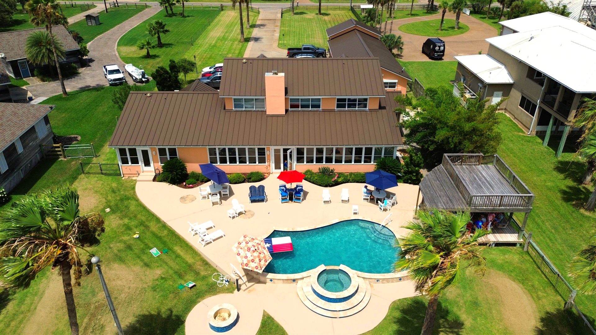Aerial view of a coastal home with backyard pool, spa, and palm trees